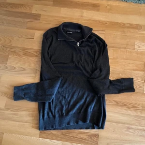 Half zip hoodie - Mörkgrå stickad tröja från Jack and Jones med halv dragkedja vid kragen. Tröjan har lång ärm och ribbade muddar vid ärmslut och nederkant. Perfekt för lager-på-lager under kyliga dagar.