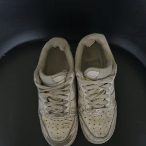 Vita Nike Air Force 1 sneakers - Klassiska vita Nike Air Force 1 sneakers med rund tå och snörning. Skorna har en platt sula och är tillverkade i syntetmaterial. Perfekta för dig som gillar streetwear och vill ha en ikonisk sneaker i garderoben.