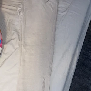 Beige mjukisbyxor från Adidas - Säljer ett par beige mjukisbyxor från Adidas med broderad logga på benet. Byxorna har resår i midjan och är tillverkade i mjuk bomull, perfekta för en avslappnad stil.
