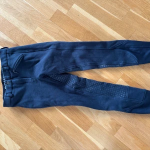 Mörkblå ridbyxor från CRW - Säljer ett par mörkblå ridbyxor från CRW som är helskodda. Byxorna har en liten dragkedjeficka fram och bälteshällor i midjan. De har varit flitigt använda, men det finns inga defekter, utom att greppet i silikonen inte är jättebra. Midjemått och innerbens längd finns med på bilder. Priset är diskuterbart! Läs bio💘