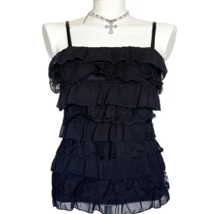 Svart volangtop med spetsdetaljer - Säljer en svart linnetopp med tunna axelband och flera lager volanger framtill. Toppen har fina spetsdetaljer mellan volangerna och är lätt transparent längst ner. Perfekt för dig som gillar en romantisk och trendig stil.