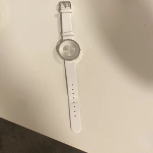 Vit klocka från Lambretta med silverfärgad urtavla - Stilren klocka från Lambretta med vitt armband och silverfärgad urtavla. Klockan har minimalistisk design och spänne i metall där Lambretta-loggan syns. 