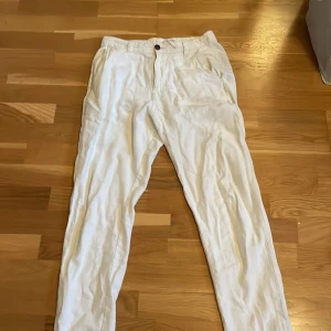Vita linnebyxor Selected home - Säljer ett par fräscha vita linnebyxor med normal passform. Byxorna har knapp och dragkedja framtill samt fickor både fram och bak. Perfekta för varma dagar och en clean stil.