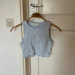Ljusblå croppad linnetopp - Säljer en ljusblå croppad linnetopp från H&M. Toppen är ribbad och ärmlös med rund halsringning, perfekt för varma dagar eller lager på lager. Enkel och stilren design som är lätt att matcha med jeans eller kjol.