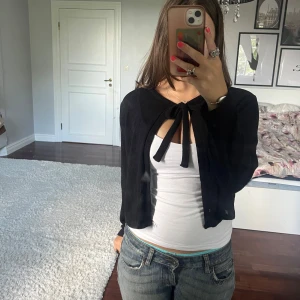 Svart stickad kofta med knyt💕 - Svart stickad kofta från Lager 157 i storlek XS. Modellen är croppad och har långa ärmar samt en snygg knytning framtill vid halsen. Perfekt att slänga över ett linne för att få en extra touch💕 Koftan är knappt använd