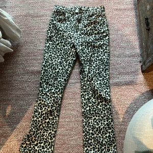 Leopardmönstrade jeansbyxor - Snygga jeansbyxor med leopardmönster i svart och beige. Klassisk femficksmodell med knapp och dragkedja framtill. Byxorna är bootcut och normal passform, perfekta för dig som vill sticka ut lite extra.