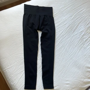 Svarta seamless leggings med hög midja - Svarta leggings med bred, ribbad och hög midja. De är sömlösa och har diskreta mönsterdetaljer längs benen för extra stilpoäng. Perfekta för träning eller chill, med stretchigt och bekvämt material som sitter snyggt på kroppen.