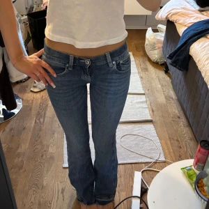 Blå bootcut jeans med broderade fickor - Säljer ett par blå bootcut jeans med snygga broderade detaljer på bakfickorna. Jeansen har låg midja och klassisk femficksdesign. Materialet är jeans i bomull och de har en lätt tvättad look. Perfekta för dig som gillar en avslappnad men ändå trendig stil. Passar mig bra i längden som 160, (skulle gissa att den är 75-76 i innerbensöämgd)