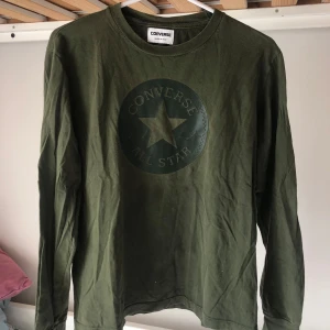 Olivgrön långärmad tröja Converse - Snygg olivgrön långärmad tröja från Converse med stort tryck av klassiska All Star-loggan på bröstet. Tröjan är i mjuk bomull och har en avslappnad passform. Ingen etikett med storlek men gissar på S/M.