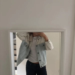 Tvåfärgad jeansjacka från M.G.B - Säljer en oversized jeansjacka från M.G.B med ljusblå denim och krämvita partier på axlar, ärmar och krage. Jackan har knappar framtill, klassiska bröstfickor och en avslappnad passform. Perfekt för dig som gillar retrovibbar och streetstyle. Den är köpt second hand!
