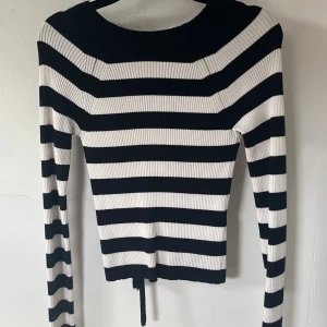 Randig ribbad topp med snörning från Zara - Säljer en svartvit ribbad topp från Zara med breda ränder och lång ärm. Toppen har snygg öppen rygg med snörningsdetalj som knyts baktill. Figurnära passform och stretchigt material, perfekt till jeans eller kjol.😌