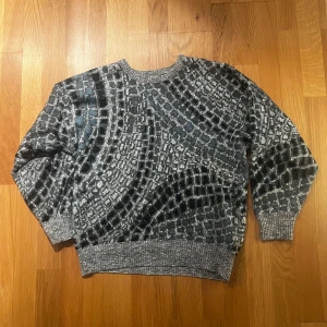 Gråmönstrad stickad tröja - Säljer en stickad tröja i olika nyanser av grått och svart med ett unikt, abstrakt mönster. Tröjan har rund halsringning, ribbade muddar och lång ärm. Perfekt för dig som vill sticka ut med en cool design.