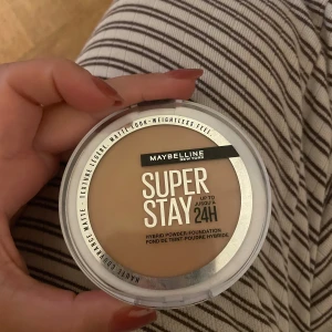 Maybelline Super Stay Foundation 40 - Maybelline Super Stay Hybrid Powder-Foundation i färgen 40 . Kompakt puderfoundation med matt finish och lätt känsla. Kommer i en rund vit dosa med spegel och applikator. Perfekt för en jämn och naturlig look som håller hela dagen.