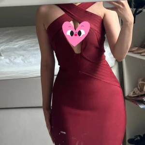 Vinröd tight bandageklänning - Säljer en vinröd tight bandageklänning med korsade axelband och djup v-ringning framtill. Klänningen är kort och figurnära med snygga detaljer i tyget som ger en lyxig känsla. Perfekt för dig som vill sticka ut och känna dig extra snygg.