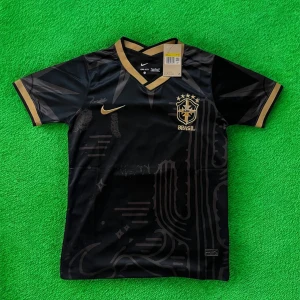 Svart Brasil Nike fotbollströja guld - Snygg svart Brasilien fotbollströja från Nike med guldiga detaljer och broderat CBF-märke på bröstet. Tröjan har V-ringning, korta ärmar och är gjord i ett lätt, snabbtorkande material. Guldiga inslag på krage, ärmslut och Nike-logga ger en riktigt exklusiv känsla.
