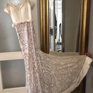 Lång spetsklänning i champagnefärg - Drömmig långklänning i champagnefärg med vackert spetsmönster och offshoulder-skärning. Klänningen har en elegant släp och romantiska detaljer i tyget. Perfekt för bal eller speciella tillfällen. Endast använd vid ett tillfälle och därefter kemtvättad.