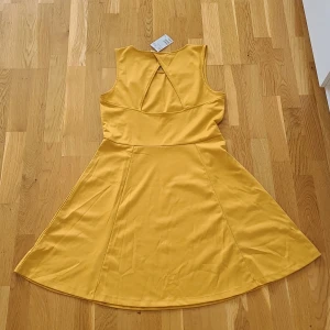Gul ärmlös klänning från H&M - Snygg gul ärmlös klänning med rund halsringning och en öppen rygg. Klänningen har en utställd kjol. Perfekt för sommaren. Helt ny, prislappen kvar. Nypris 99 kr. 