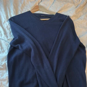 Mörkblå stickad tröja från Mywearman - En klassisk mörkblå stickad tröja från Mywearman i storlek S. Tröjan har v-ringad hals, långa ärmar och ribbade muddar vid ärmslut och nederkant. Perfekt för lager-på-lager och enkel att matcha med jeans eller chinos.