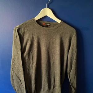 Grå tröja i pima bomull från Dressmann - En stilren grå långärmad tröja från Dressmann i mjuk pima bomull. Klassisk rund halsringning och enkel design som funkar till allt. Perfekt för dig som gillar basic och bekvämt med en clean look.