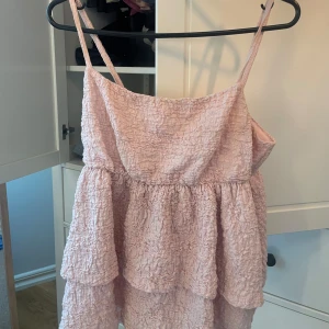 Ljusrosa volangtopp Gina Tricot - Supersöt ljusrosa kort blus från Gina Tricot med smala axelband och flera volanger. Toppen har en krinklad struktur och är perfekt för varma dagar. Lätt och luftig modell som ger en romantisk vibe.