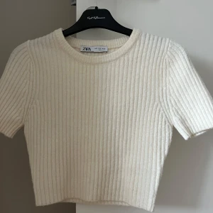 Ribbad croppad tröja från Zara - Superfin ribbad croppad tröja från Zara i offwhite. Tröjan har korta ärmar, rund halsringning och är stickad i ett mjukt material. Perfekt till jeans eller kjol för en clean och trendig look. 