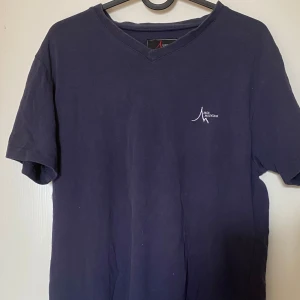 Mörkblå t-shirt  - En stilren mörkblå t-shirt från High Mountain med v-ringad hals och diskret logga på bröstet. Klassisk passform och korta ärmar, perfekt till jeans eller shorts. Skön bomullskänsla och enkel att matcha. Frakt tillkommer