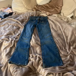 Blå bootcut jeans från Kappahl. - Snygga blå jeans från Kappahl i storlek 158. Modellen har bootcut-ben, klassiska fickor fram och bak samt coola detaljer med ficklock och knapp framtill. Jeansen är i mjukt denimtyg och passar perfekt till en avslappnad stil.