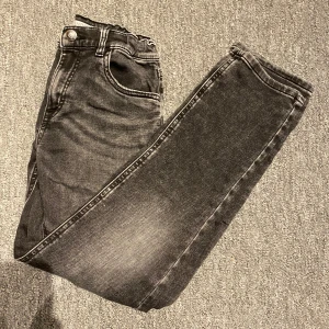 Svarta jeans - Snygga svarta jeans med lätt tvättad look och stretchig passform. Klassisk femficksmodell med dragkedja och knapp framtill. Perfekta för dig som gillar en modern stil. Den har en liten slitning där nere men som ej märks när dom används.