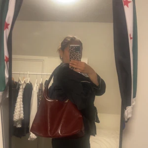 Vinröd axelväska i skinn - Säljer en stor och rymlig vinröd axelväska i glansigt skinn. Väskan har en enkel, mjuk form med bred axelrem och ljus insida. Perfekt för dig som vill ha plats för allt du behöver under dagen. Stilren och snygg att bära över axeln.