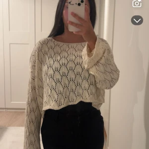 Beige stickad croppad tröja - Säljer en beige stickad tröja med snyggt hålmönster och croppad passform. Tröjan har vida, långa ärmar och en rund halsringning. Perfekt för lager-på-lager och ger en chill men ändå söt vibe. Supersnygg och knappast snvänd. Onesize