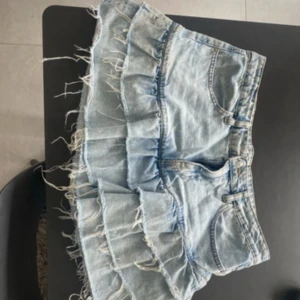 Ljusblå jeanskjol med volanger -  PRIS KAN DISKUTERAS!! Supersöt ljusblå jeanskjol med volanger och råa kanter. Kjolen har klassiska fickor fram och bak, samt en cool, fransig look som ger en avslappnad vibe. Perfekt för dig som vill sticka ut med en trendig och lekfull stil.