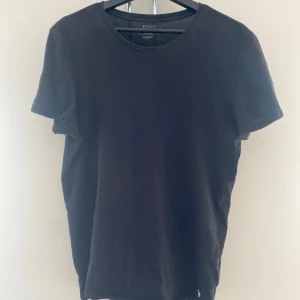 Svart Ralph Lauren T-shirt - Klassisk svart t-shirt från Polo Ralph Lauren med rund hals och korta ärmar. Tillverkad i mjuk bomull och har den ikoniska broderade loggan i vitt längst ner. Enkel och stilren modell som funkar till allt.