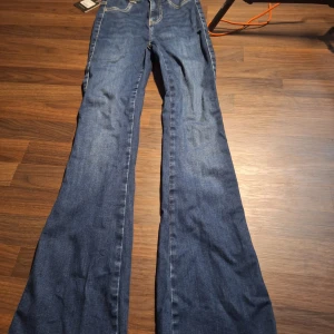 Blå flared jeans från FitJeans S - Snygga blå flared jeans från FitJeans i modellen Sapphire Blue. Jeansen har utsvängda ben, klassisk femficksdesign och kontrastsömmar. Perfekta för dig som gillar en retro vibe och vill sticka ut med en cool siluett.