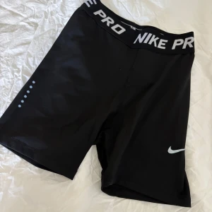 Nike Pro svarta träningstights shorts - Svarta Nike Pro shorts i tight modell med stretch resår i midjan där det står NIKE PRO i vitt. Tillverkade i Dri-FIT syntetmaterial som andas, perfekt för träning. Swoosh-logga på benet och diskreta prickdetaljer på sidan. Sitter skönt och följsamt. Shortsen är stretch bara och väldigt bekväma! Endast använda en gång så i mycket bra skick