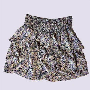 Blommig kjol från Vero moda - Supersöt blommig, kort kjol från Vero moda. Lila, gula och gröna blommor. Stretchig i midjan. Storlek S. Mycket fint skick! Endast använd ett fåtal gånger.