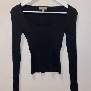 Svart ribbad tröja från H&M - Svart ribbad långärmad tröja från H&M med fyrkantig urringning och tight passform. Ärmarna har en snygg slits vid handleden som ger en extra detalj. Perfekt att styla med jeans eller kjol för en clean look.