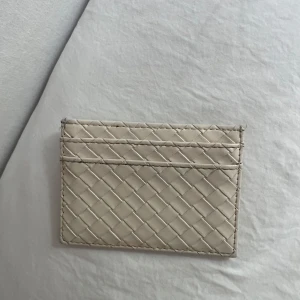 Beige flätad korthållare i skinn - Säljer en stilren beige korthållare i flätat skinn. Den har flera fack för kort och är superenkel att ha med sig i fickan eller väskan. Perfekt för dig som gillar minimalistisk och clean design.