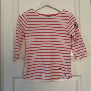 Randig tröja från Hampton Republic - Vit och röd randig tröja från Hampton Republic med trekvartsärm och rund hals. Snygg detalj med Sail and Yachting Club-märke på ena ärmen. Perfekt för en chill och stilren look. Gjord i mjuk bomull som känns skön mot huden.