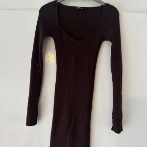 Brun ribbad klänning Gina Tricot XS - Mörkbrun ribbad kortklänning från Gina Tricot med lång ärm och v-ringad hals. Klänningen är tight och har en snygg, figurnära passform som framhäver siluetten. Perfekt för dig som gillar stilrena och enkla plagg med en twist.