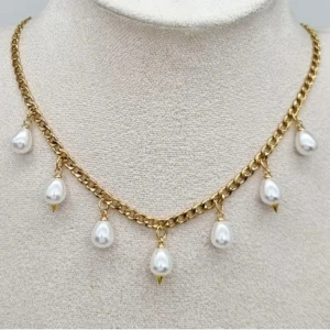 Guldhalsband med pärlhängen - Snyggt halsband i guldton med sju droppformade vita pärlor som hänger längs kedjan. Kedjan är grov och ger en cool kontrast till de eleganta pärlorna. Perfekt för att lyfta din outfit med lite extra bling och stil.