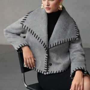 Grå kappa med bred krage från Motf - Säljer en grå kappa från Moit med bred, markerad krage och svarta dekorativa sömmar längs kanterna. Jackan har två knappar för att stänga. Nypris: 1000