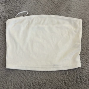 Vit bandeau tubtopp - Säljer en enkel och fräsch vit bandeau tubtopp i mjuk ribbad bomull. Toppen är ärmlös och har en clean look som är perfekt till varma dagar. Passar dig som gillar minimalistisk stil och vill ha en basic topp i garderoben.