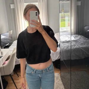 Svart croppad tröja med puffärm - Svart croppad tröja med rund hals och puffiga kortärmar. Enkel och stilren design som passar perfekt till jeans eller kjol. Snyggt avslut vid midjan för en trendig look.