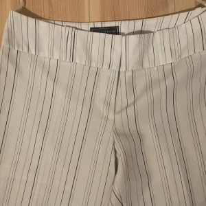 Randiga vita bootcut-byxor - Snygga vita bootcut-byxor från Mashrum med svarta och grå tunna ränder. Byxorna har bred linning och fickdetaljer bak. Skulle säga att dem är storlek S/M