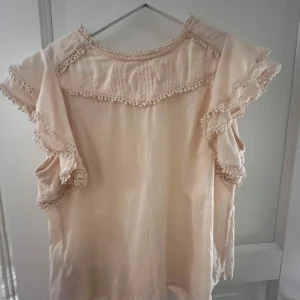 Beige blus med spets från Mango - Supersöt beige blus från mango med volangärmar och spetsdetaljer längs kanterna. Blusen har rund hals och är tillverkad i mjukt bomullstyg. Perfekt för dig som gillar romantiska och boho vibes. Passar dig som vill ha en chill och feminin look.