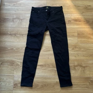 Stretchiga byxor Lee - Svarta och stretchiga byxor i jeanslikt tyg från Lee. Två fickor både fram och bak. Storlek: 30/31. Material: 65% bomull, 17% polyester, 18% viskos och 2% elastan. Inte så använda, bra skick!
