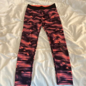 Mönstrade leggings från H&M - Snygga träningsbyxor från H&M i storlek 158/164 med ett coolt abstrakt mönster i svart, rött och orange. De har en bred svart midja och är gjorda i ett stretchigt syntetmaterial som sitter tight och bekvämt. Perfekta för träning eller chill.
