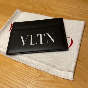 Svart Valentino Garavani plånbok - Snygg svart plånbok från Valentino Garavani med VLTN-tryck i vitt på framsidan. Slimmad design med plats för kort, tillverkad i exklusivt skinn. Kommer med originalförpackning och dustbag. Perfekt för dig som gillar stilrena accessoarer med lyxig känsla. Kvitto FINNS!, skriv om du har några funderingar?