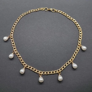 Guldhalsband med droppformade pärlor - Snyggt halsband i guldtonad kedja med sju droppformade vita pärlor som hänger längs länkarna. Kedjan har en chunky look och pärlorna ger en elegant touch. Perfekt för dig som vill sticka ut med en unik accessoar.