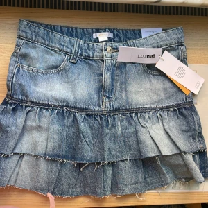 Blå jeanskjol med volanger Gina Tricot - Säljer en blå low waist jeanskjol från Gina Tricot med låg midja och coola råa kanter. Kjolen har två lager volanger och klassiska fickor fram och bak. Perfekt för dig som gillar en trendig och avslappnad denimlook. Är i nyskick med prislappen kvar på, använd 0 ggr då de är för stora för mig. Hör av dig vid frågor 
